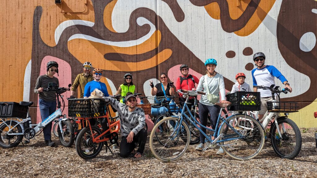 A group of cyclists posing in front of a modern mural.